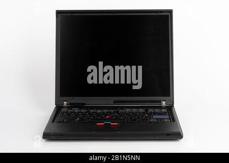 Old laptop on white background, which was produced in 2005, outer cover reinforced titanium, metal hinges, red trackpoint. Stock Photo