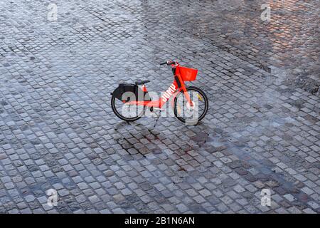 PARIS, FRANCE - FEBRUARY 26, 2020:  JUMP red dockless electric bike acquired by Uber parked ditched right in the middle of a wet cobblestoned place. Stock Photo