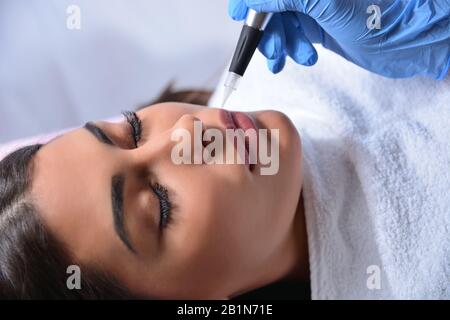 Cosmetologist applying permanent makeup on woman lips in beauty studio with a professional tattoo tool. Beauty and micro pigmentation concept Stock Photo