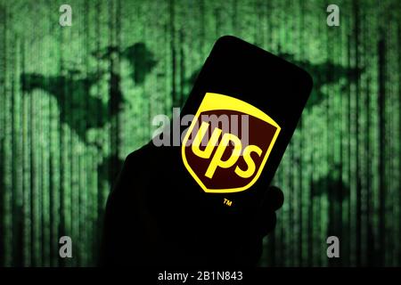 UPS shipping company logo seen displayed on smart phone screen with Matrix-like world map visible blurred in the background Stock Photo