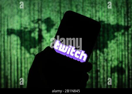 Twitch streaming website logo seen displayed on smart phone screen with Matrix-like world map visible blurred in the background Stock Photo