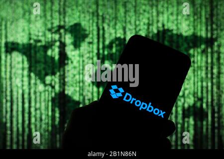 Dropbox online cloud company logo seen displayed on smart phone screen with Matrix-like world map visible blurred in the background Stock Photo