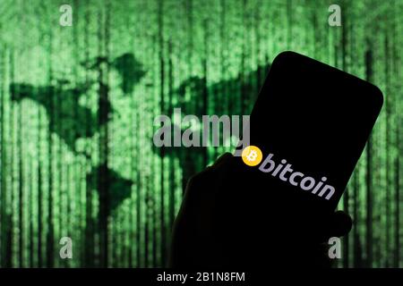 Bitcoin cryptocurrency logo seen displayed on smart phone screen with Matrix-like world map visible blurred in the background Stock Photo