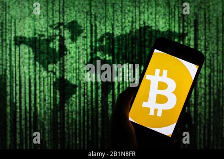 Bitcoin cryptocurrency logo seen displayed on smart phone screen with Matrix-like world map visible blurred in the background Stock Photo