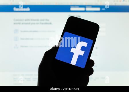Facebook company logo seen displayed on smart phone screen with Facebook welcome screen visible blurred in the background Stock Photo