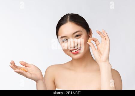 Young attractive asian woman who takes a capsule or pill. Isolated over white background. Stock Photo