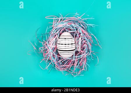 Graphic hand-painted in line egg in decorative nest on blue pastel background. Easter concept. Stock Photo