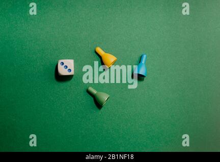 Three playing chips next to hard shadows and a white playing cube with the number 3 on a flat plain green background, clean background, top view, flat Stock Photo