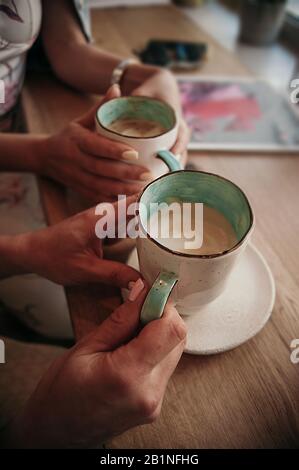 a pair of women's hands with a beautiful delicate pastel manicure hold ceramic mugs white on the outside mint inside with coffee and milk foam on the Stock Photo