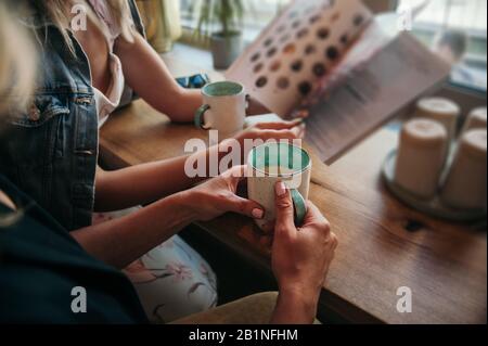 a pair of women's hands with a beautiful delicate pastel manicure hold ceramic mugs white on the outside mint inside with coffee and milk foam on the Stock Photo