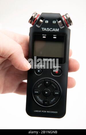 HUETTENBER, GERMANY - FEBRUARY 03, 2020: Male Hand hold Tascam DR-05X Digital Audio recorder. Portable field recorder on white desk. Stock Photo