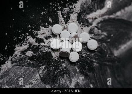 scattered white small tablets on a scattered white powder on a black flat background top view macro Stock Photo