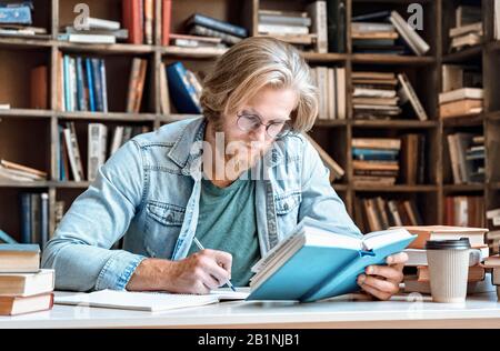 Focused young man in glasses sit library desk make notes education concept. Stock Photo