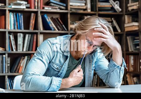 Serious smart focused student glasses library desk think on task solve problem. Stock Photo
