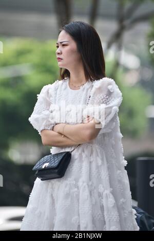 Wuhan: A young woman with a white dress and a black purse waiting at the exit of Chuhe Hanije metro station, Zhong Bei Lu street. China Stock Photo
