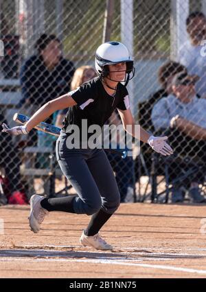 Female high school softball player flinging the bat aside as she postures to spint up the first base line. Stock Photo