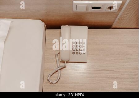 not a modern white wired telephone with buttons on a beige wooden bedside table Stock Photo