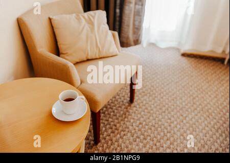 stylish interior in warm colors, an easy chair with a pillow and white tea utensils on the table, a place for a home office or a place to relax Stock Photo