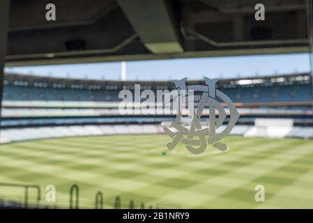 The Melbourne Cricket Club (MCC) logo on a glass door in the MCG Members bar with the field being readied for a cricket match in the background Stock Photo