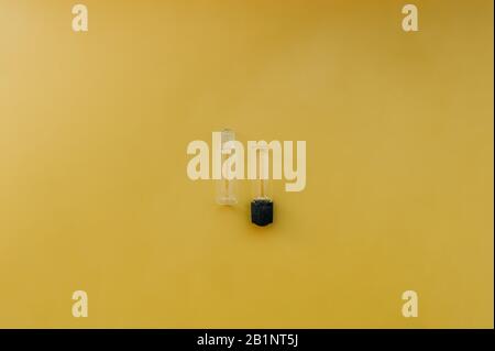 two small empty transparent jar with a black lid for cosmetology or medicine on a uniform bright yellow background Stock Photo