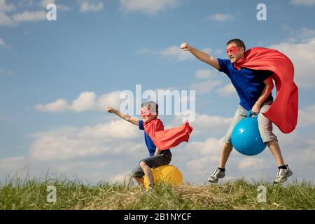 Father and son playing superhero at the day time. People having fun outdoors.They jumping on inflatable balls on the lawn. Concept of friendly family. Stock Photo