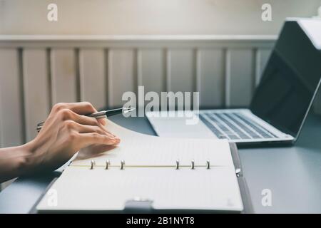 Closeup of woman's hand holding a pen on notebook. Freelance journalist working at home. Stock Photo
