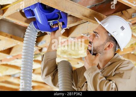 tradesman pondering how to pass ventilation system through ceiling Stock Photo