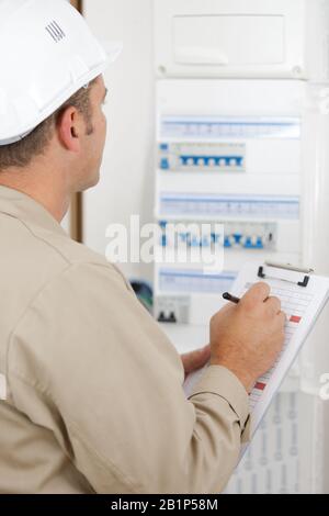 electrician worker checking clipboard while working in fuse-board Stock Photo