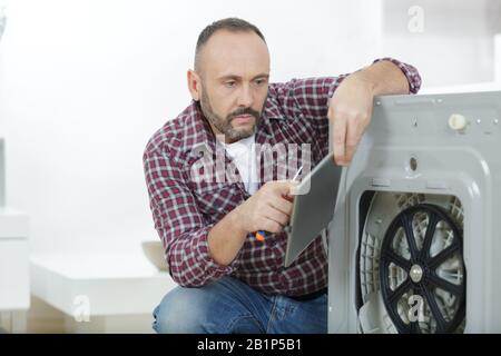 serviceman holding tablet while repairing washing machine Stock Photo