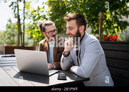 Positive successful business specialists discussing plan with laptop outdoors. Stock Photo