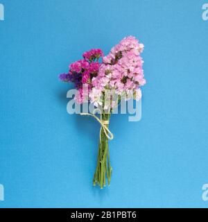 Pink purple statice flowers bouquet on blue background. Floral composition, flat lay, top view Stock Photo