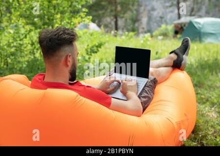young man with laptop working on nature. Freedom, remote work, freelancer, technology, internet, travel and vacation concepts. Stock Photo