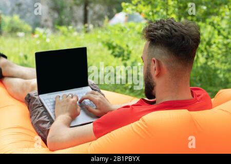 Fit travel blogger writing article on black laptop screen. Freelance remote work concept. Self employed man coding. Stock Photo
