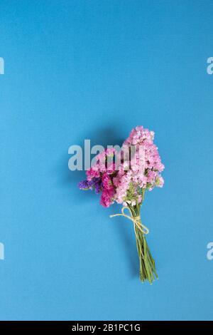 Pink purple statice flowers bouquet on blue background. Floral composition, flat lay, top view Stock Photo