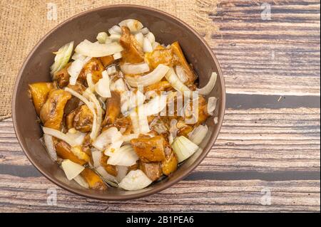 Salted mushrooms with onions in a ceramic bowl on a wooden background. Homemade preparations, rustic treats. Close up Stock Photo
