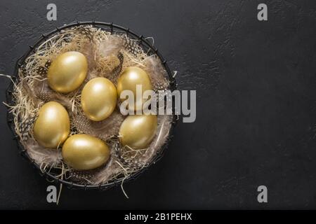 Chicken colored golden eggs in decorative vase on black background. Easter dark concept. Top view and copy space. Stock Photo