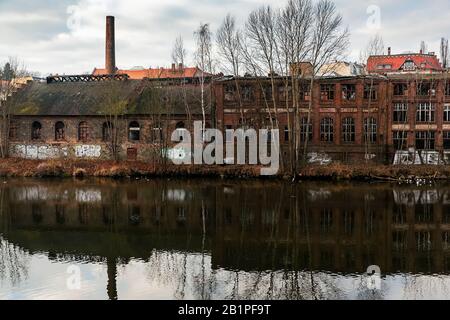 Buildings of an abandoned factory in Görlitz on the river Neisse. broken windows, damaged walls. Reflection of the facade in the river Stock Photo