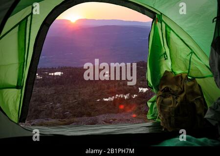 View from inside a tourist tent with backpack. Beautiful Scandinavian landscape of sunset and mountains. Norway Stock Photo