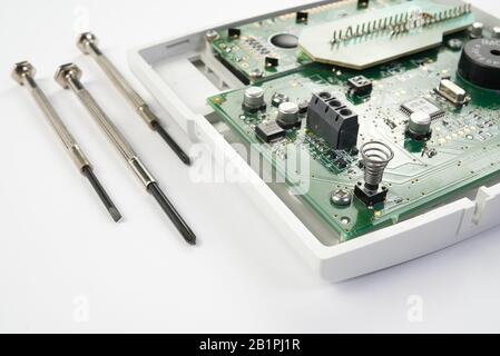 Home alarm control panel repairing. Open Electronic board panel with screwdrivers on a white background. Stock Photo