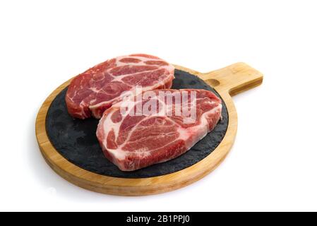 two raw pork slices on black stone plate, isolated on white. Stock Photo