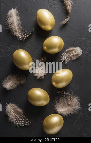 Chicken colored golden eggs and feathers on black. Easter dark concept. View from above. Easter composition. Spring. Stock Photo