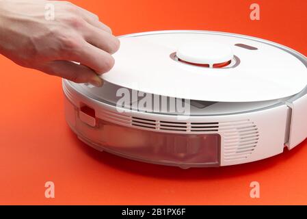 Robot vacuum cleaner, cleaning the trash bin and cleaning the filter. Robot vacuum cleaner isolated on red background. Stock Photo
