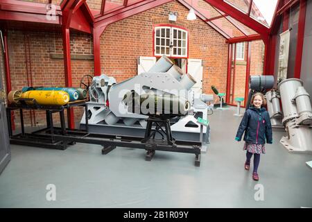 Young child tourist girl kid visitor walking past a Squid mortar system which was a British World War II ship-mounted anti-submarine weapon. Shown at the Explosion Museum of Naval Firepower which is based at the Royal Navy's former armaments depot of Priddy's Hard, in Gosport. UK (105) Stock Photo