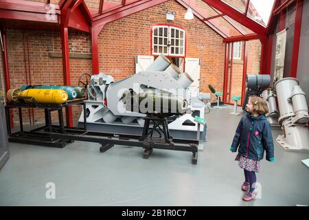 Young child tourist girl kid visitor walking past a Squid mortar system which was a British World War II ship-mounted anti-submarine weapon. Shown at the Explosion Museum of Naval Firepower which is based at the Royal Navy's former armaments depot of Priddy's Hard, in Gosport. UK (105) Stock Photo