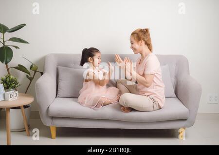 Side view portrait of little girl playing clapping game with mom sitting on sofa together Stock Photo