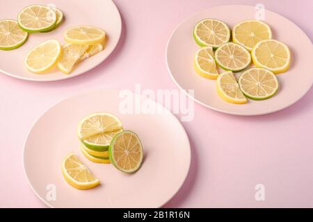 Fresh tasty lemon and lime citrus fruits slices on three pink plates, minimal background isolated, angle view Stock Photo