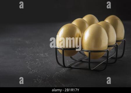 Chicken golden eggs in stand on black background. Easter dark concept. Close up. Copy space. Stock Photo