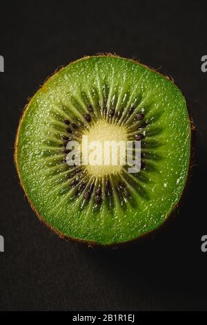 Kiwi fruit half sliced on dark black plain background, macro photography close up Stock Photo