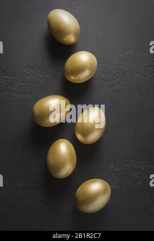 Chicken colored golden eggs on black. Easter creative dark concept. View from above. Minimal composition. Stock Photo