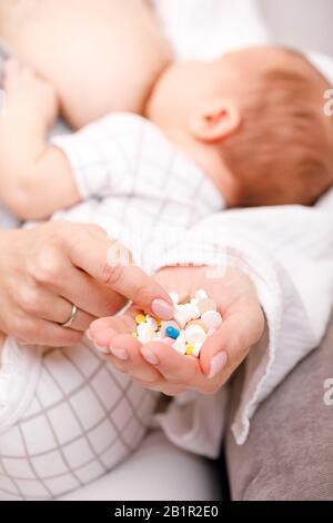 Mother holding handful of pills and tablets while breastfeeding newborn baby. Breastfeeding and medication concept Stock Photo